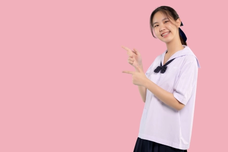 Happy braces asian student girl in school uniform finger pointing on isolated pastel background